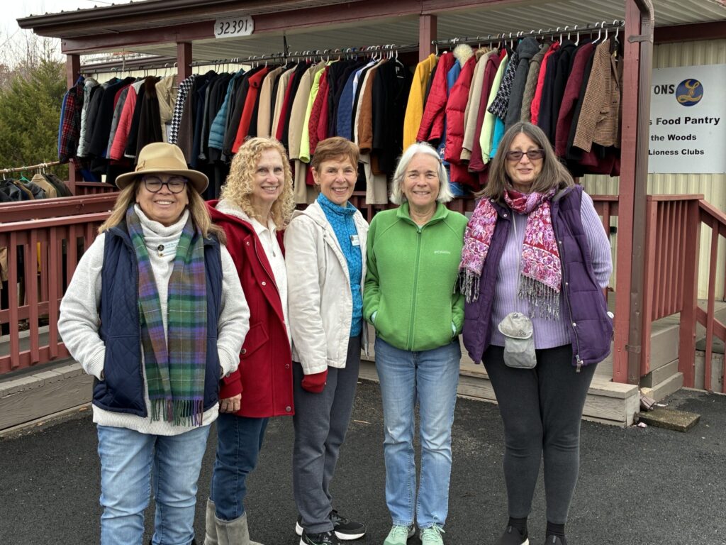 Five women smile in front of a clothing donation rack at a food pantry