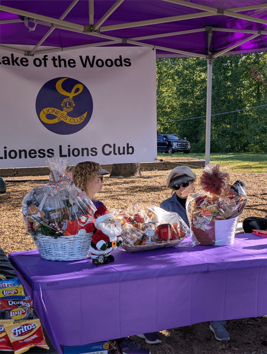 Two women at a table under a purple canopy display holiday gift baskets for the Lake of the Woods Lioness Lions Club